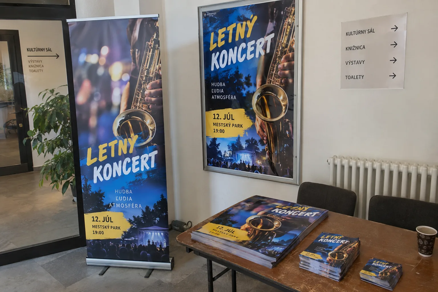 Ilustračná fotografia hotových plagátov mestského kultúrneho podujatia v rôznych formátoch a roll-upu pri odovzdaní.